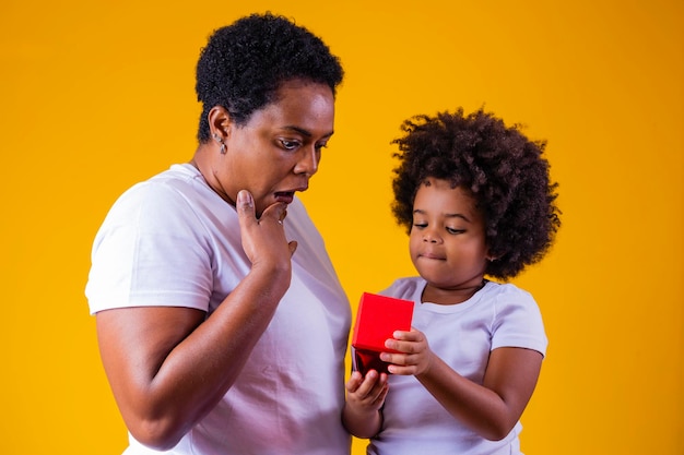 Concept de la fête des mères Adorable enfant de sexe féminin tenant le cadeau de la fête des mères Portrait d'une maman heureuse afro et de sa petite fille ravie du cadeau qu'elle a reçu