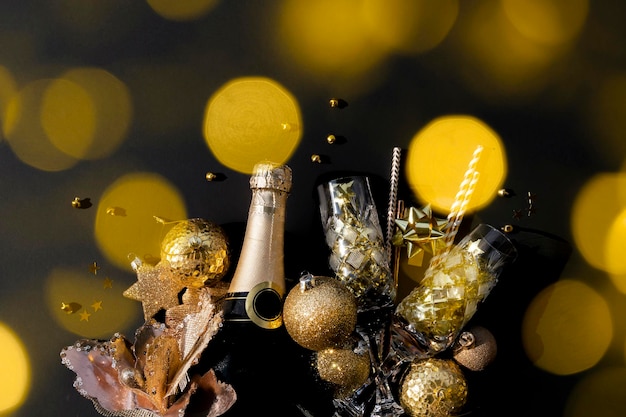 Concept de fête de Noël ou du nouvel an à plat d'une bouteille de champagne avec des confettis de verres en cristal, des boules et des pailles sur fond noir