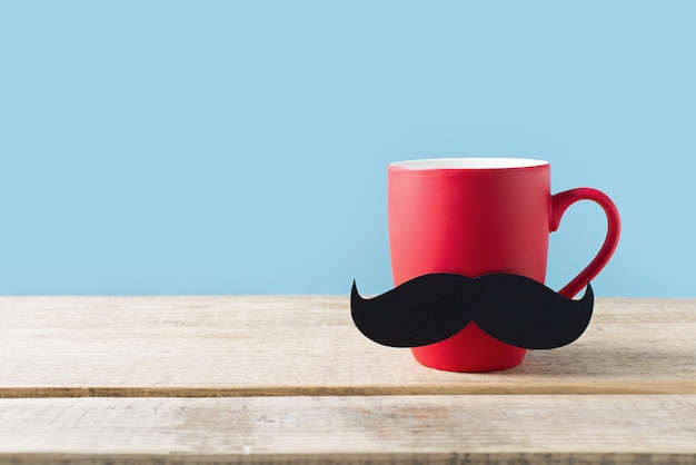 Concept de fête des pères avec une tasse rouge et moustache sur fond bleu