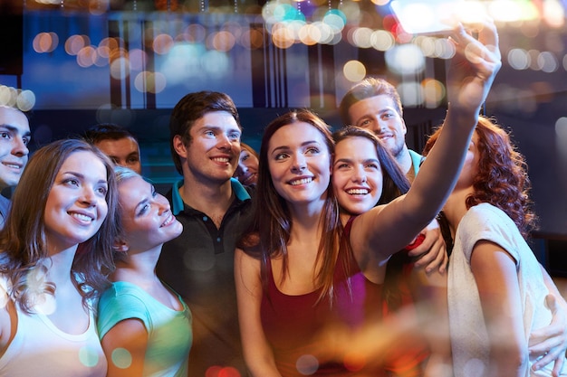 concept de fête, de technologie, de vie nocturne et de personnes - amis souriants avec un smartphone prenant un selfie dans un club