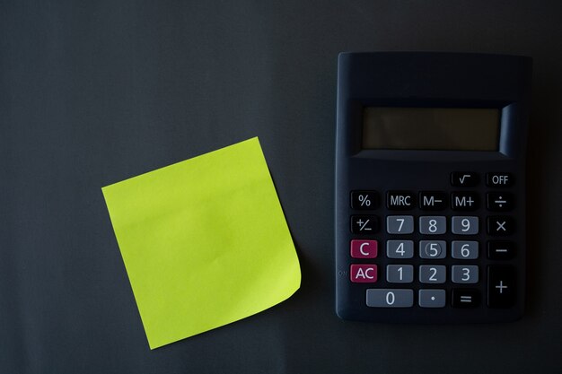 Concept de finances, papier de rappel et calculatrice sur fond noir