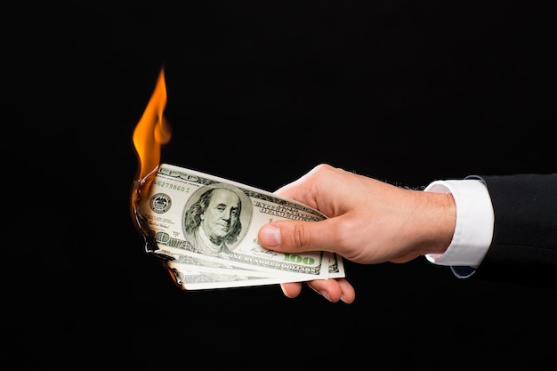 concept de finances, de personnes, d'épargne et de faillite - gros plan d'une main masculine tenant de l'argent en dollars brûlant sur fond noir
