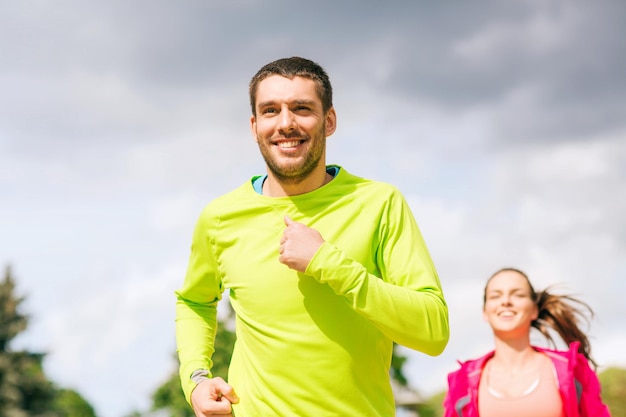 concept de fitness, de sport, d'amitié et de style de vie - couple souriant courant à l'extérieur