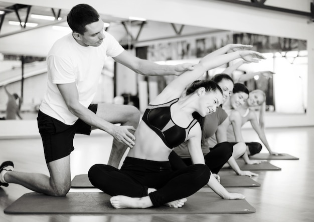 concept de fitness, sport, entraînement, gym et style de vie - groupe de femmes souriantes avec un entraîneur masculin s'étirant sur des tapis dans la salle de gym
