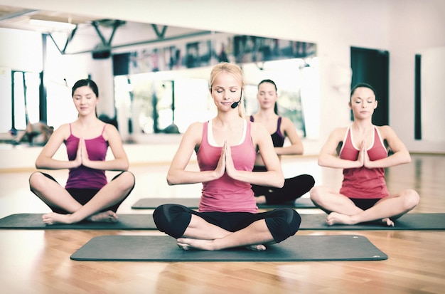 concept de fitness, sport, entraînement, gym et style de vie - groupe de femmes souriantes avec entraîneur méditant dans une pose de yoga