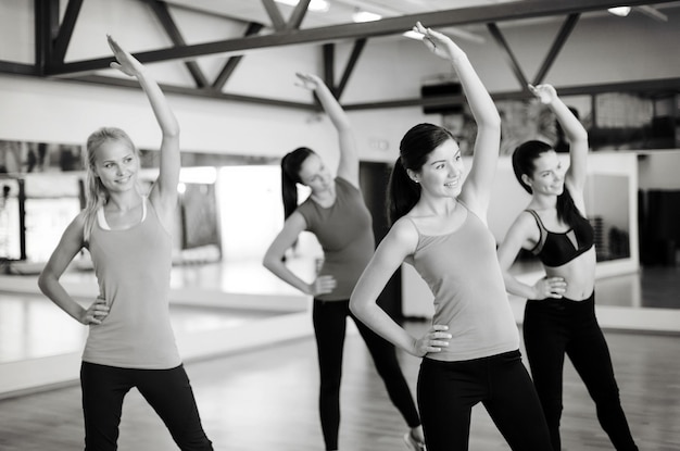 concept de fitness, sport, entraînement, gym et style de vie - groupe de personnes souriantes s'étirant dans la salle de gym