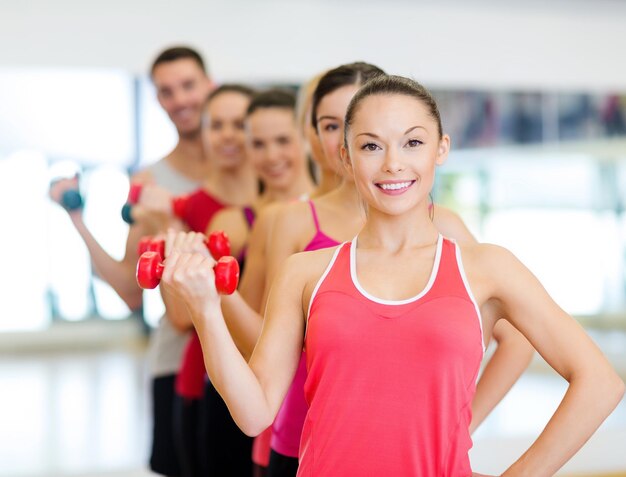 concept de fitness, sport, entraînement, gym et style de vie - groupe de personnes souriantes soulevant des haltères dans la salle de gym