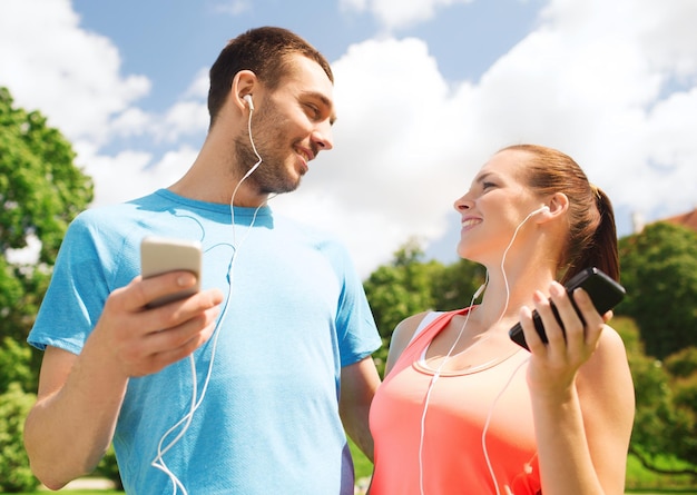 concept de fitness, de sport, d'entraînement, de technologie et de style de vie - deux personnes souriantes avec des smartphones et des écouteurs à l'extérieur