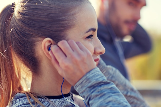 concept de fitness, de sport, de personnes, de technologie et de style de vie - couple heureux à l'extérieur et écouter de la musique dans les écouteurs