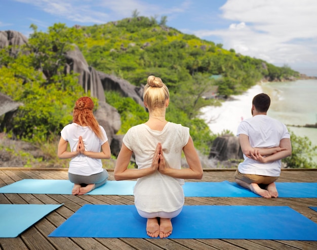 Photo concept de fitness, de sport, de yoga et de mode de vie sain - un groupe de personnes faisant de l'exercice dans une posture de prière inversée sur le fond d'une plage tropicale
