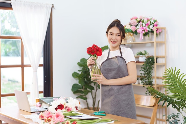 Concept de fleuriste Femme fleuriste tenant un vase de gerbera rouge pour préparer l'envoi au client en magasin