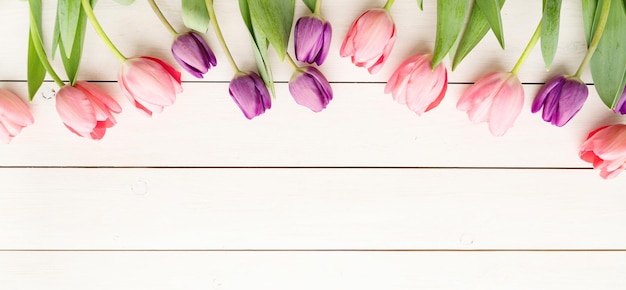 Concept de fleurs de printemps tulipes roses et violettes sur une table en bois blanche bannière de fond