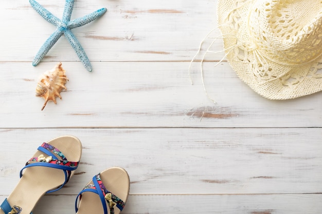 Concept de fond d'été sandales féminines, étoile de mer, coquillages, chapeau de paille sur une surface en bois clair