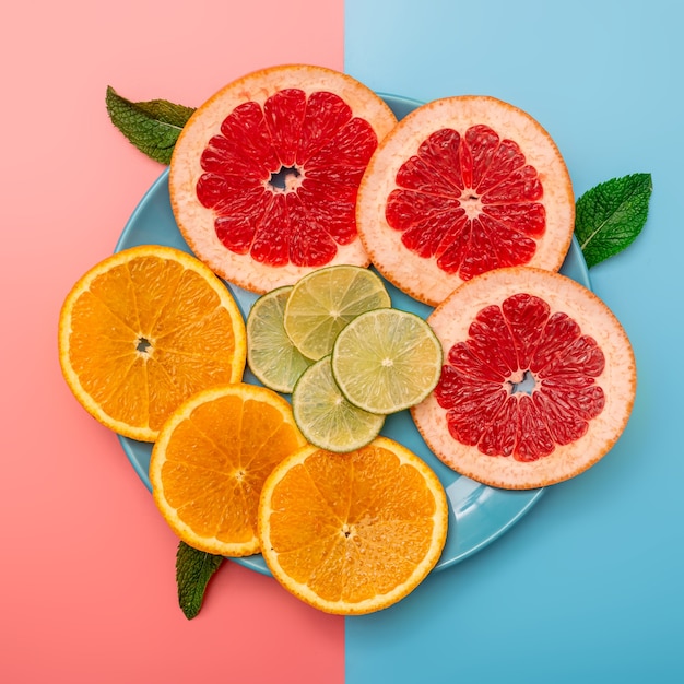 Concept de fond d'été en tranches d'orange, pamplemousse, citron, citron vert sur fond rose et bleu