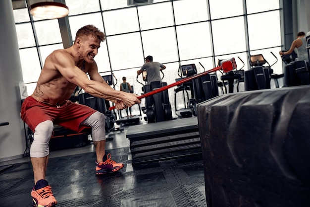 Concept de force Athlète masculin utilisant un marteau pendant l'entraînement de remise en forme Homme de remise en forme battant un pneu en caoutchouc dans une salle de sport