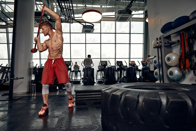 Concept de force Athlète masculin utilisant un marteau pendant l'entraînement de remise en forme Homme de remise en forme battant un pneu en caoutchouc dans une salle de sport