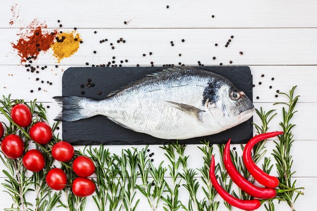 Concept de fruits de mer méditerranéens. Poisson Dorado cru avec tomates et romarin sur table en bois blanc. Haut