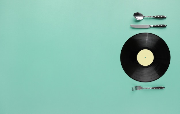 Concept de goût de la musique avec disque vinyle comme plaque avec couteau et fourchette sur fond pastel abstrait
