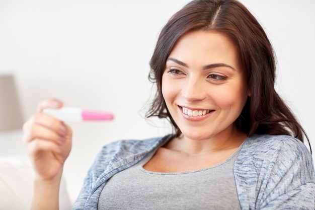 concept de grossesse, de fertilité, de maternité et de personnes - femme souriante heureuse regardant un test de grossesse à la maison