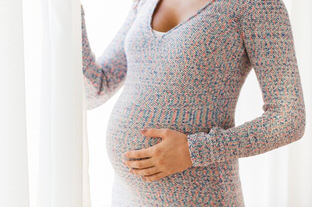 concept de grossesse, de maternité, de personnes et d'attentes - gros plan d'une femme enceinte avec un gros ventre regardant vers la fenêtre