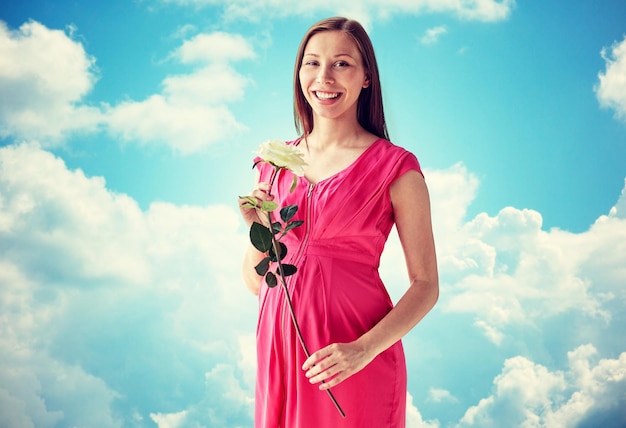 concept de grossesse, de maternité, de personnes, de vacances et d'attente - femme enceinte heureuse avec une fleur de rose blanche sur fond bleu ciel et nuages