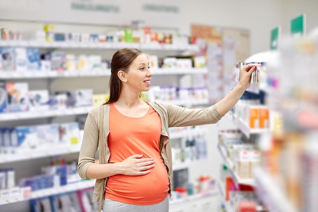 concept de grossesse, de médecine, de pharmacie, de soins de santé et de personnes - femme enceinte heureuse choisissant des médicaments à la pharmacie