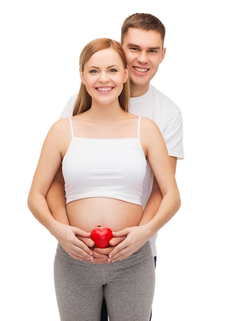concept de grossesse, de parentalité, d'amour et de bonheur - jeune famille heureuse attend un enfant avec un petit coeur rouge