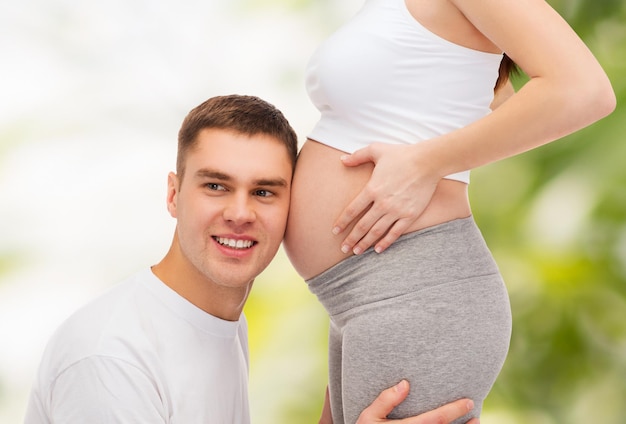 concept de grossesse, de parentalité et de bonheur - père heureux écoutant le ventre de sa femme enceinte