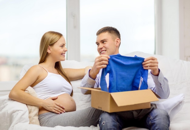 concept de grossesse, de poste, d'accouchement et de parentalité - famille heureuse attendant un enfant assis sur un canapé et ouvrant une boîte à colis avec un cardigan bleu