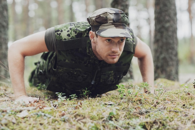 concept de guerre, d'armée, d'entraînement et de personnes - jeune soldat ou ranger portant l'uniforme militaire faisant des pompes dans la forêt