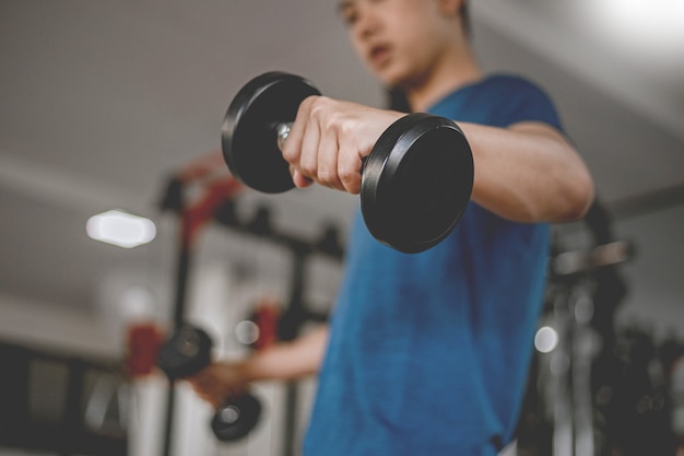 Concept de gym d'entraînement un jeune adulte utilisant son bras musclé et puissant soulevant un haltère vers le haut et vers le bas dans la salle de gym.