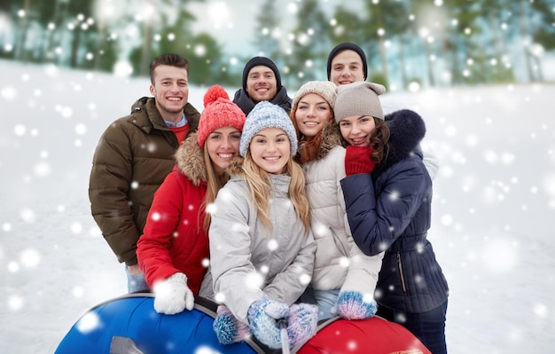 concept d'hiver, de loisirs, d'amitié, de technologie et de personnes - groupe de jeunes hommes et femmes souriants avec des tubes à neige prenant des photos avec un bâton de selfie de smartphone à l'extérieur