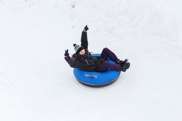 concept d'hiver, de loisirs, de sport et de personnes - adolescent ou jeune homme heureux glissant sur un tube à neige et montrant le geste de la victoire