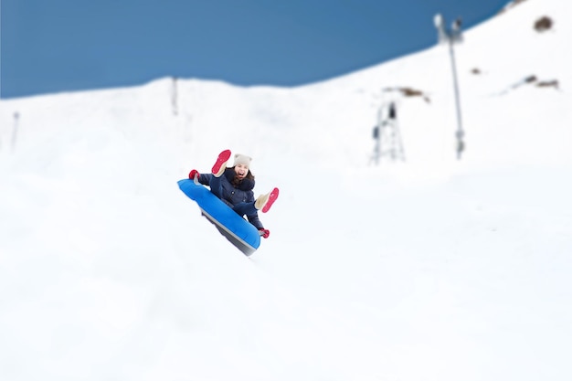 concept d'hiver, de loisirs, de sport et de personnes - adolescente ou femme heureuse glissant sur un tube à neige sur fond de montagne