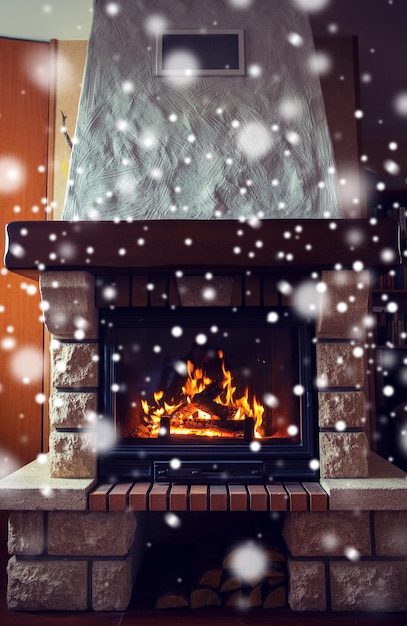 Photo concept d'hiver, de noël, de chaleur, de feu et de confort - gros plan d'une cheminée en feu à la maison avec de la neige