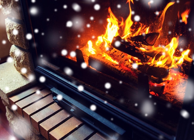 concept d'hiver, de noël, de chaleur, de feu et de confort - gros plan d'une cheminée en feu à la maison avec de la neige