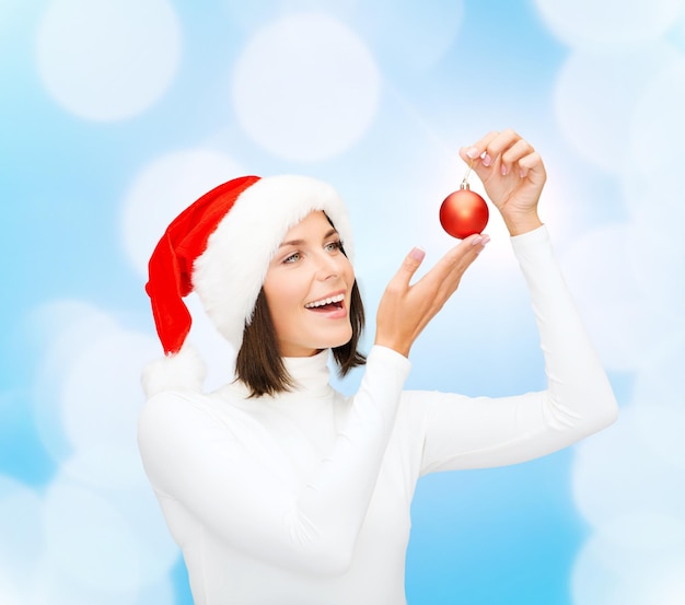 Photo concept d'hiver, de personnes, de noël et de bonheur - femme en chapeau de santa helper avec boule de décoration d'arbre de noël sur fond de lumières bleues