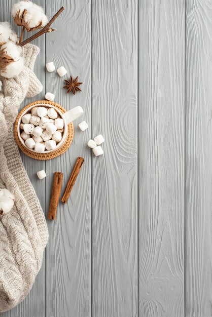 Photo concept d'hiver vue de dessus photo verticale d'une tasse de boisson chaude avec de la guimauve sur un napperon en rotin branche de coton écharpe tricotée confortable bâtons d'anis et de cannelle sur fond de bureau en bois gris