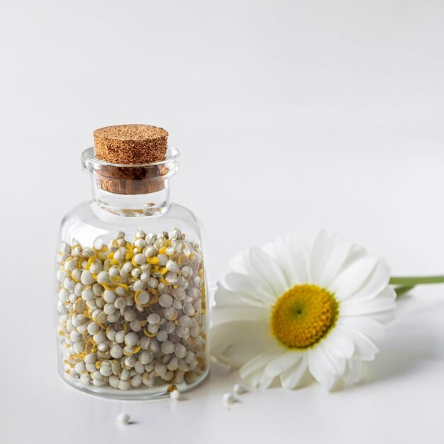 Concept homéopathique Camomille dans un flacon transparent et grains homéopatiques sur un fond blanc