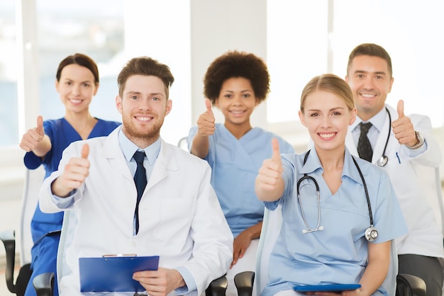 concept d'hôpital, de profession, de personnes et de médecine - groupe de médecins heureux lors d'un séminaire dans une salle de conférence à l'hôpital montrant le geste du pouce levé