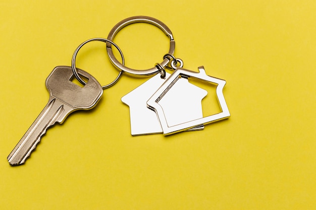 Le concept d'hypothèque et de logement locatif et immobilier. Prêt de crédit hypothécaire. Porte-clés en forme de maison avec une clé sur fond jaune.