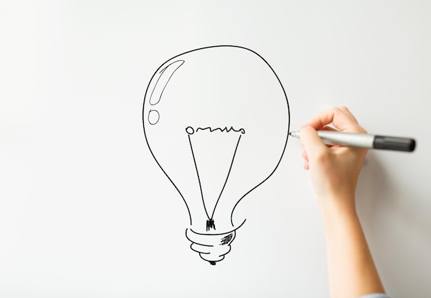 concept d'idée, d'inspiration, d'entreprise, de personnes et d'éducation - gros plan de la main avec un marqueur dessinant une ampoule sur un tableau blanc ou un mur