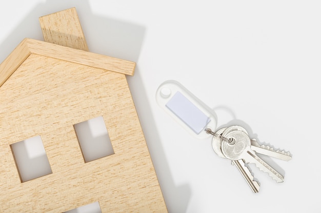 Photo concept immobilier. icône de la maison avec des clés sur fond blanc. maquette. copiez l'espace. vue de dessus