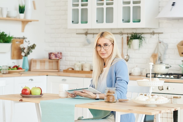 Concept indépendant. Belle femme d'affaires dans des vêtements décontractés et des lunettes examine des documents et souriant tout en travaillant avec un ordinateur portable dans la cuisine