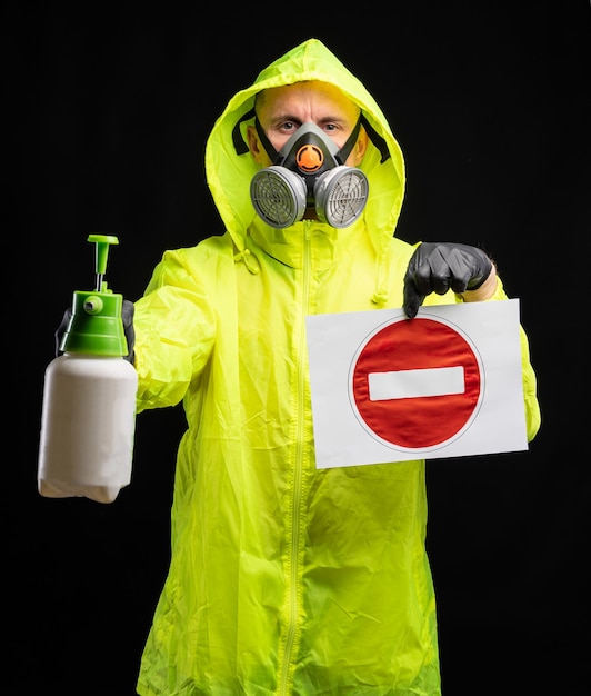 Photo concept d'infection par le coronavirus covid-19. homme dans un respirateur de protection et des gants tenant un liquide désinfectant et un panneau d'arrêt sur fond noir