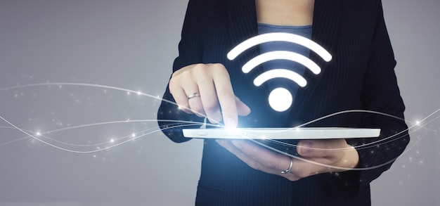 Concept Internet de technologie de signal de réseau WiFi gratuit. Tablette blanche en main de femme d'affaires avec signe Wi-Fi hologramme numérique sur fond gris. Concept de connexion réseau d'entreprise.