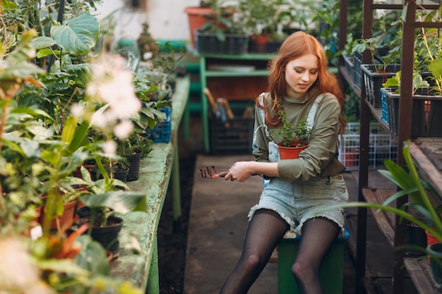 Concept de jardinage à domicile. Jeune jolie femme avec râteau assis à planter des plantes. Plante de jardin maison de printemps.