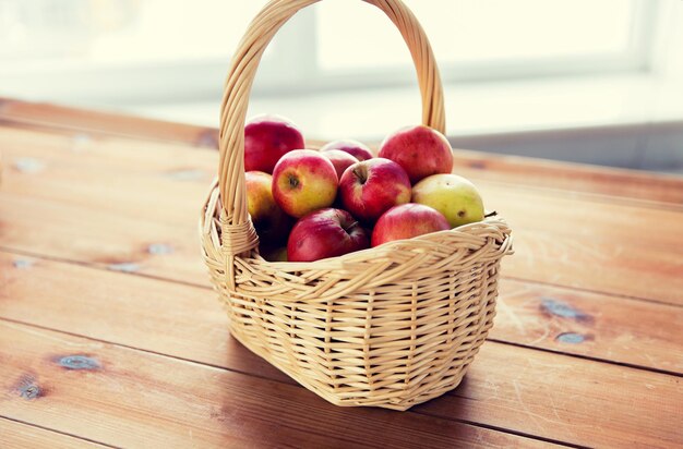 concept de jardinage, de saison, d'automne et de fruits - gros plan d'un panier en osier avec des pommes rouges mûres sur une table en bois