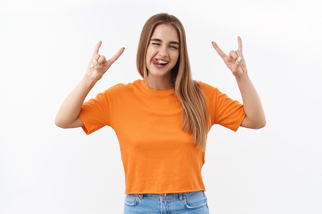 Concept de jeunesse, de jeunesse et de style de vie. Portrait d'une fille caucasienne blonde heureuse et insouciante s'amusant lors d'un festival ou d'un concert, montrant la langue et le heavy-metal, signe rock-n-roll, profitant de la fête