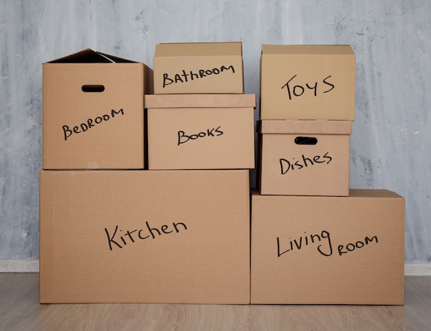 Concept de jour de déménagement - pile de boîtes en carton marron avec des objets domestiques sur fond de mur gris